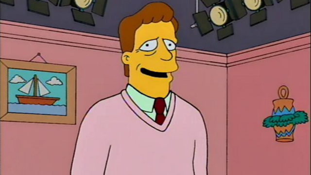 Troy McClure stands in a TV set version of the Simpsons' lounge room