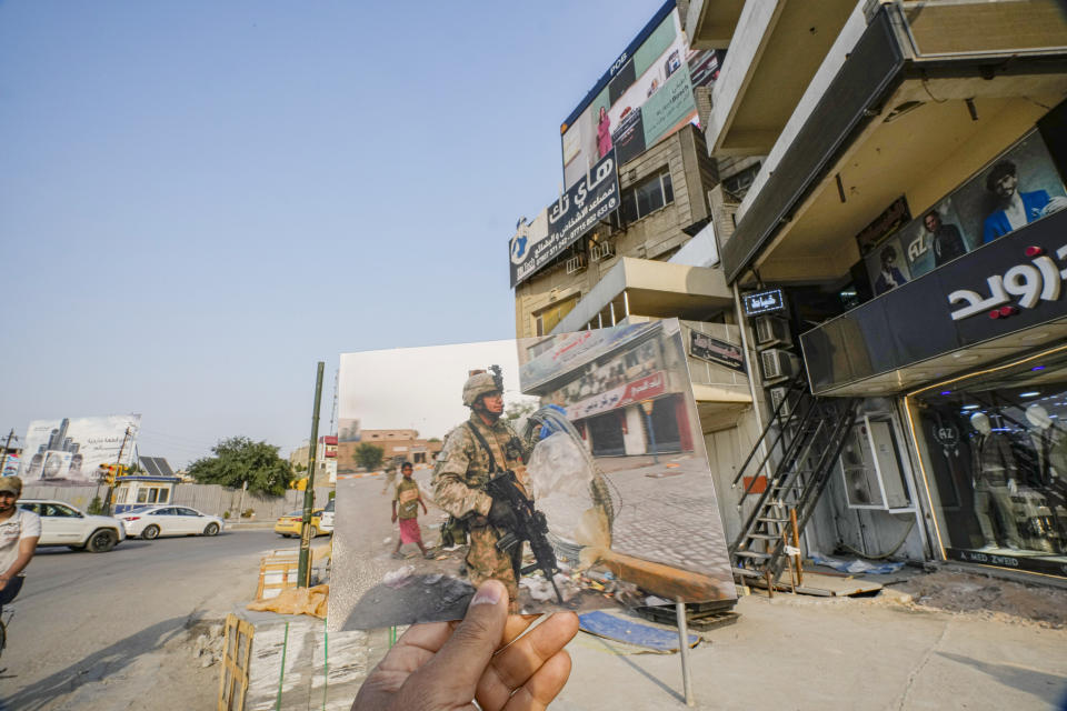 A photograph of a 172nd Stryker Brigade Combat Team soldier removing barbed wire after the troops ended search for a missing soldier in Baghdad's Karradah neighborhood Tuesday, Oct. 31, 2006, iis inserted into the scene at the same location on Friday, March 24, 2023. 20 years after the U.S. led invasion on Iraq and subsequent war. (AP Photo/Hadi Mizban)