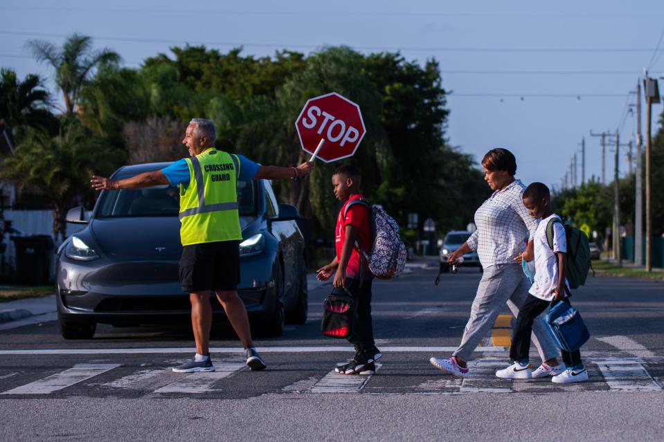 Delray Beach resident Kattly Nelson crosses Northwest Third Terrace with her twin 8-year-old boys, Bryan, left, and Ryan Nelson, as crossing guard Oscar Saturno holds up a stop sign to traffic during the first day of school at S.D. Spady Elementary School in Delray Beach, FL., on Wednesday, August 10, 2022.