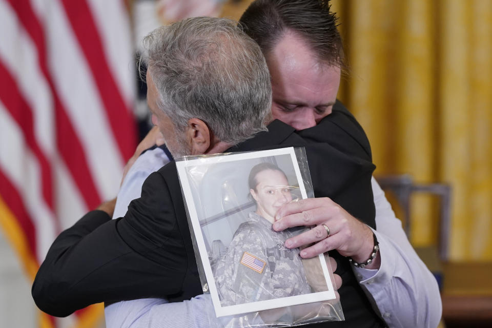 FILE - Activist and entertainer Jon Stewart hugs Sri Benson, husband of Katie Benson who served in Kuwait and died of mesothelioma, as they arrive to attend an event where President Joe Biden will sign the "PACT Act of 2022" in the East Room of the White House, Aug. 10, 2022, in Washington. Hundreds of thousands of veterans have received additional benefits in the past year after President Joe Biden signed legislation expanding coverage for conditions connected to burn pits that were used to destroy trash and potentially toxic materials. (AP Photo/Evan Vucci, File)