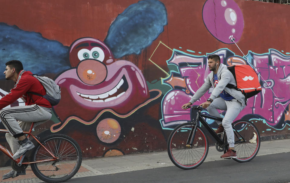 Venezuelan bicycle courier Samuel Romero pedals past murals in Bogota, Colombia, Wednesday, July 17, 2019. The 21-year-old migrant turns on his phone and logs on to Rappi, an app through which freelance cyclists get paid to make deliveries around the traffic-clogged city of 8 million. (AP Photo/Fernando Vergara)