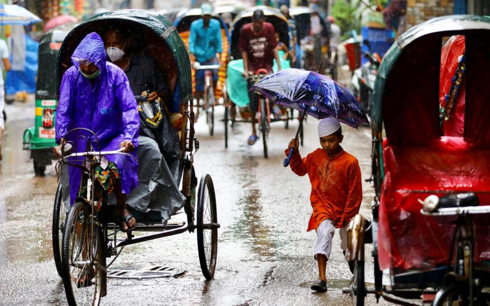 Commuters on a street during rain in Dhaka - Mohammad Ponir Hossain/Reuters