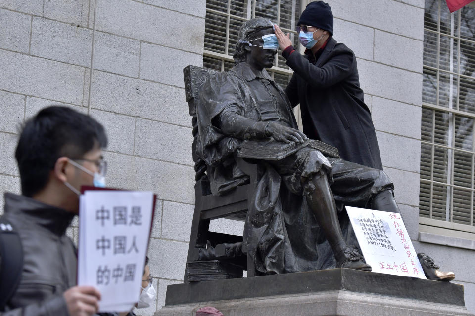 A man places a mask over the eyes of the John Harvard Statue in Harvard Yard as dozens of students and faculty demonstrate against strict anti-virus measures in China, Tuesday, Nov. 29, 2022, at Harvard University in Cambridge, Mass. Protests in China, which were the largest and most wide spread in the nation in decades, included calls for Communist Party leader Xi Jinping to step down. (AP Photo/Josh Reynolds)