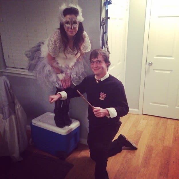 A woman in an owl costume standing on a cooler next to a kneeling guy in a sweater and glasses