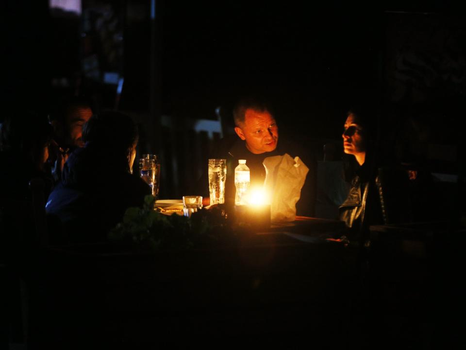 A group of people eat dinner illuminated by candlelight.