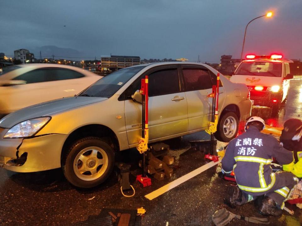 疑似因天雨，陳姓女子騎機車不慎自撞汽機車道間的防撞桿，摔倒後遭後方疾駛而來的自小客車輾過壓在車底，經消防人員採用撐頂拉撐開器等破壞器材救出送醫仍告不治。（消防局提供）