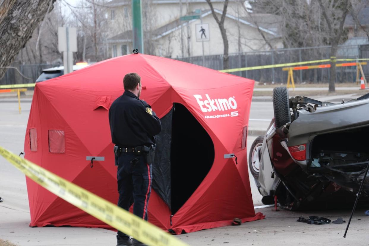 A Saskatoon Police Service officer is beside an upside down vehicle with a red tent popped up beside it, and debris scattered on April 14, 2024. (Liam O'Connor/CBC - image credit)