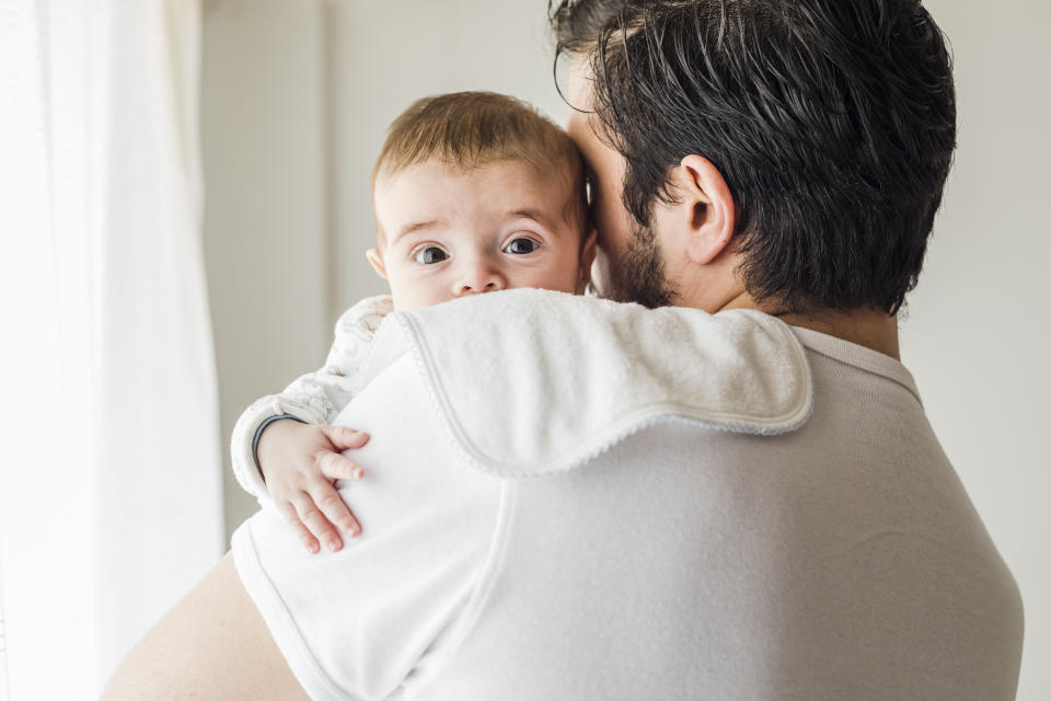 Father burping his baby in bedroom, after being breastfed.