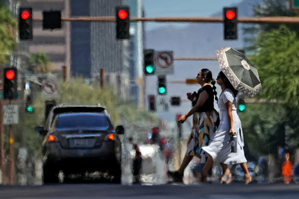 Dos mujeres cruzan una calle el lunes 17 de julio de 2023 en el centro de Phoenix, mientras ondas de calor envuelven a la ciudad. (AP Foto/Matt York)