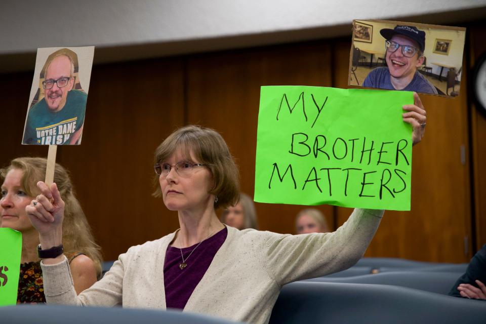 Laura McLellan, sister of a resident of Portage Manor, holds up signs showing pictures of her brother at the County-City Building in South Bend, on June 14, 2023.