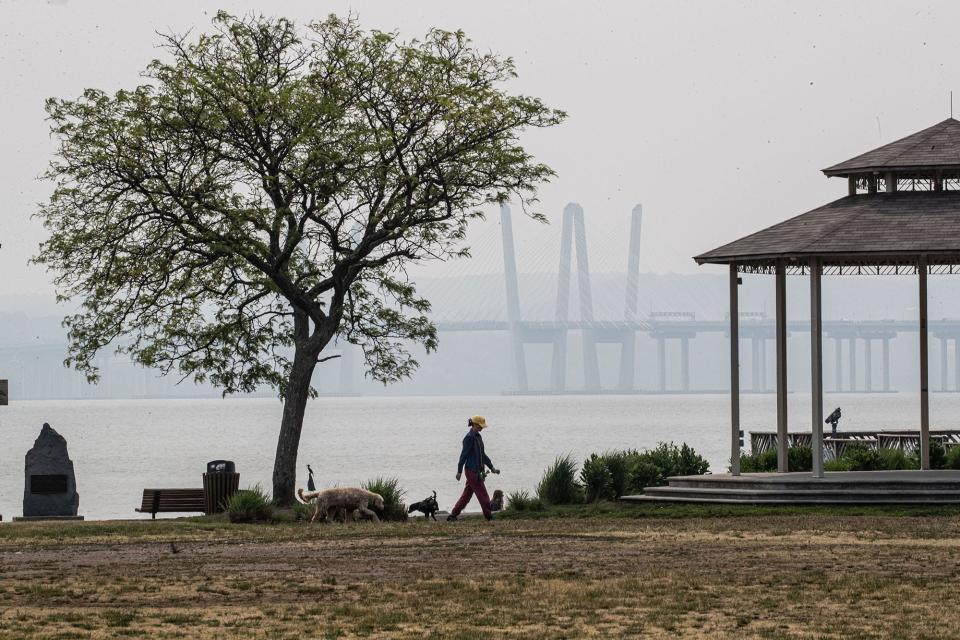 With the Gov. Mario M. Cuomo Bridge over the Hudson River obscured by haze, a woman walks her dog in Memorial Park in Nyack June 7, 2023. Much of the northeastern United States was under air quality alerts due to smoke from hundreds of wildfires in Canada. 