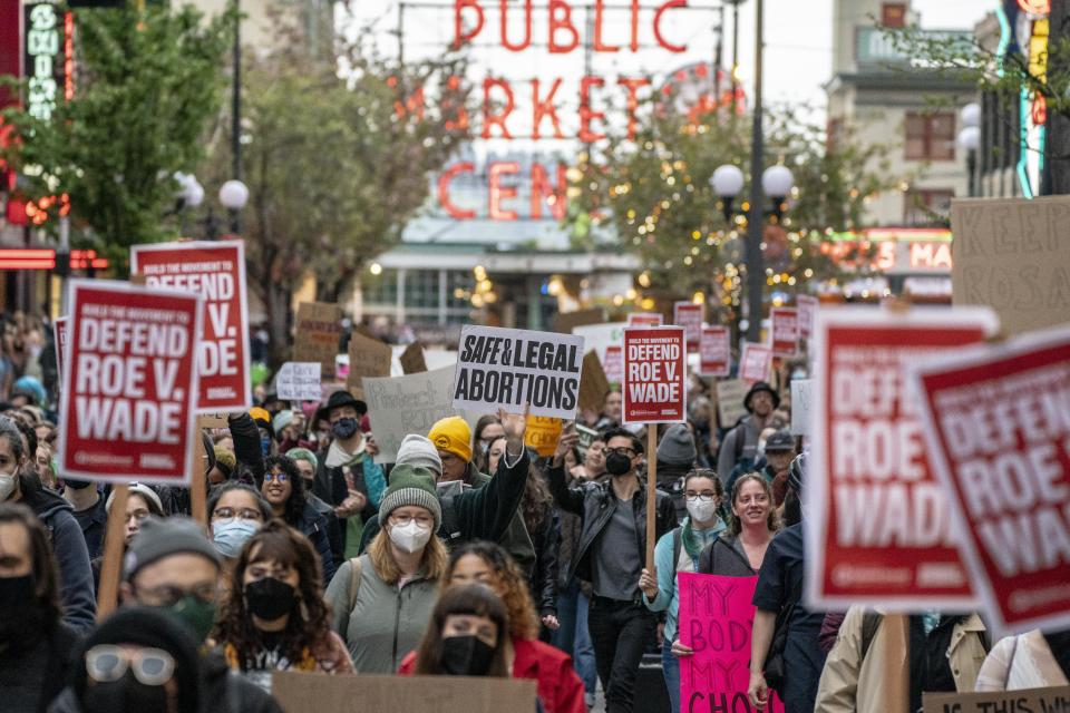 Demonstrators, many wearing masks, carry banners saying: Defend Roe v. Wade and Safe & Legal and My Body, My Choice.