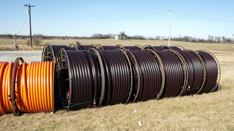 Large drums of fiber optic cable sitting in a field, with a barn and silo in the background.