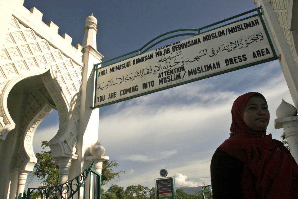 FILE - In this Sept. 13, 2009 file photo, a Muslim woman walks past beneath a sign advising people to wear Muslim attire at Baiturrahman Grand Mosque in Banda Aceh, Aceh province, Indonesia. An Indonesian woman who was gang-raped by men who accused her of having extramarital sex may be caned publicly for violating Islamic law, an official said Wednesday, May 7, 2014. The 25-year-old widow said she was raped by eight men who allegedly found her having sex with a married man in her house. The men reportedly beat the man, doused the two with sewage, and then turned them over to Islamic police in conservative Aceh province. Indonesia, the world's most populous Muslim nation of 240 million people, has a policy of secularism but allows Aceh, a predominantly Muslim province on the northern tip of Sumatra, to implement a version of Sharia Islamic law. (AP Photo/Heri Juanda, File)