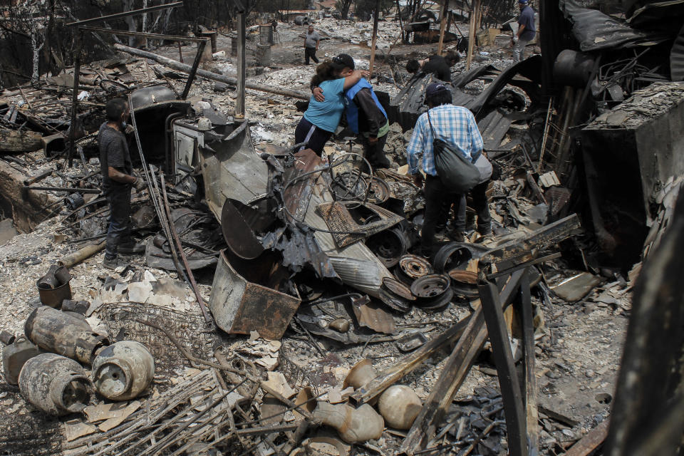 Locals embrace each other amidst debris and burnt-out houses after forest fires reached their neighborhood in Vina del Mar, Chile, Sunday, Feb. 4, 2024. (AP Photo/ Cristobal Basaure)