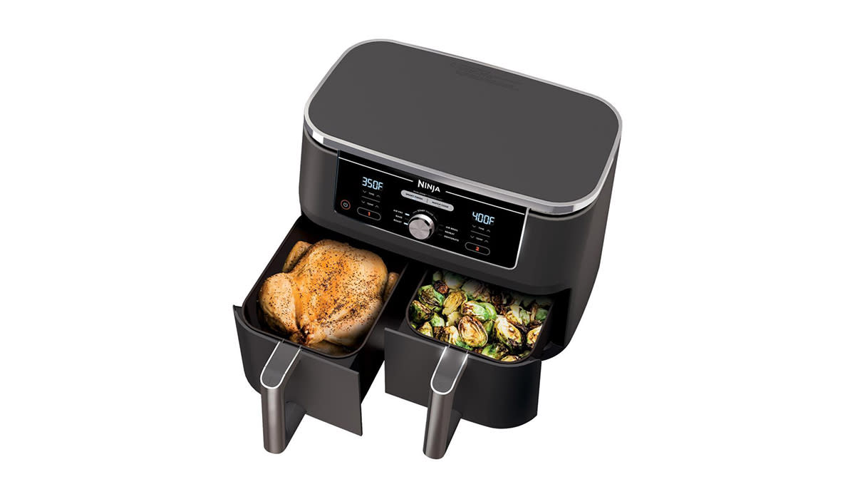 Black air fryer shown from above with both baskets open. One on the left has a whole chicken inside and the one on the right has roasted Brussels sprouts