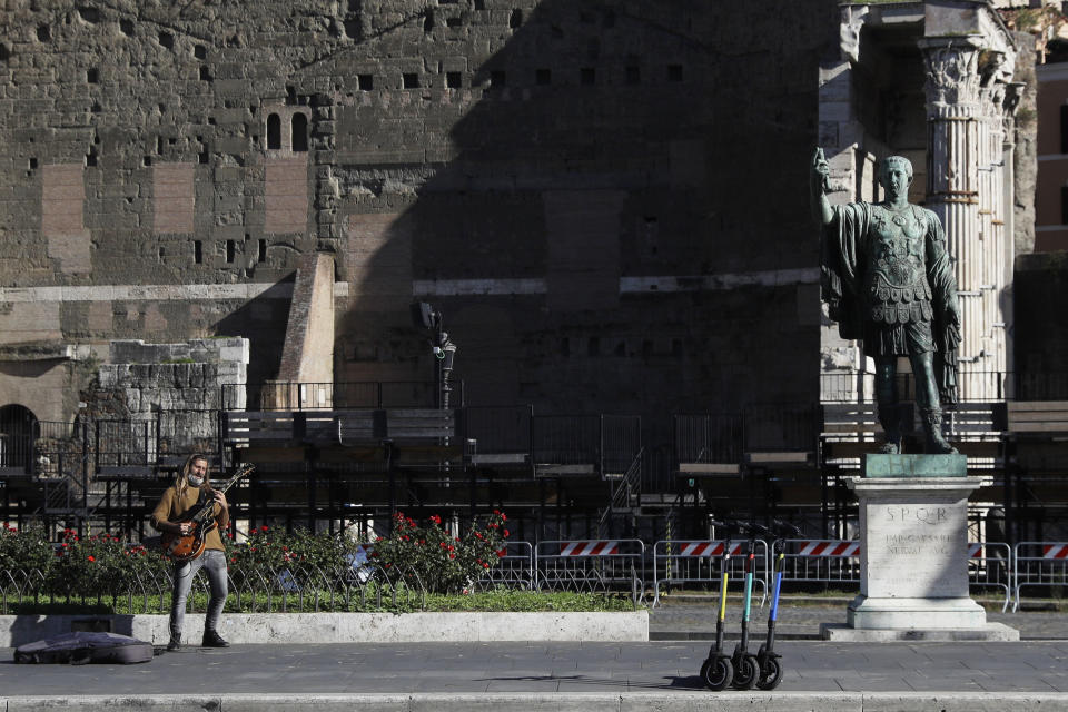 A street musician performs with his electric guitar beside the statue of Roman Emperor Julius Cesar on a almost empty Via Dei FOri Imperiali avenue in Rome, Wednesday, Oct. 28, 2020. Italy on Tuesday registered nearly 22,000 confirmed COVID-19 infections since the previous day, its highest one-day total so far in the pandemic. The day-to-day increase in confirmed deaths also jumped, to 221, according to Health Ministry figures. (AP Photo/Gregorio Borgia)