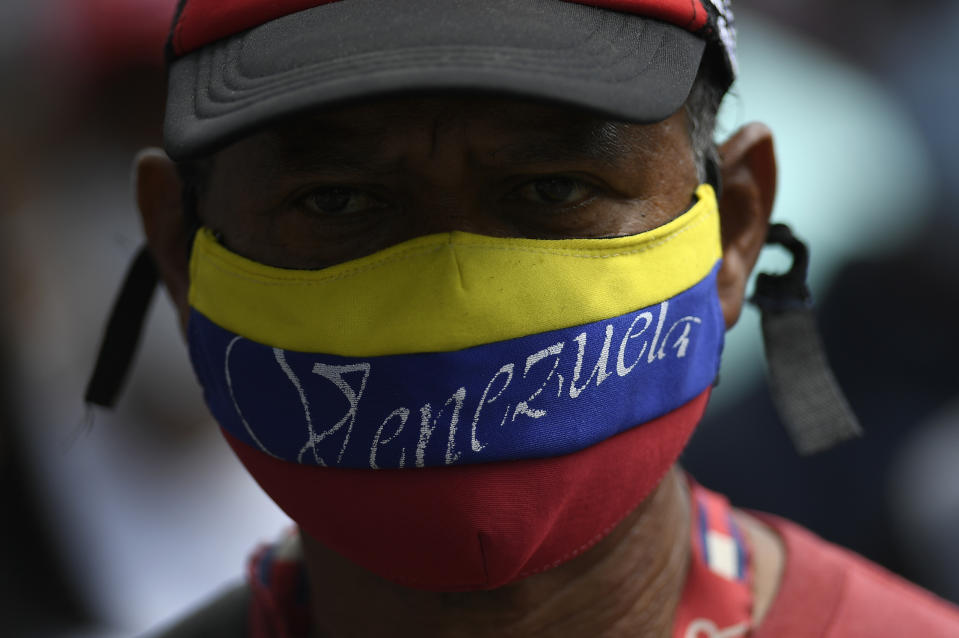 A government supporter, wearing a mask with the colors of the national flag, takes part in a march marking Youth Day, in Caracas, Venezuela, Saturday, Feb. 12, 2022. The annual holiday commemorates the young people who accompanied heroes in the battle for Venezuela's independence. (AP Photo/Matias Delacroix)