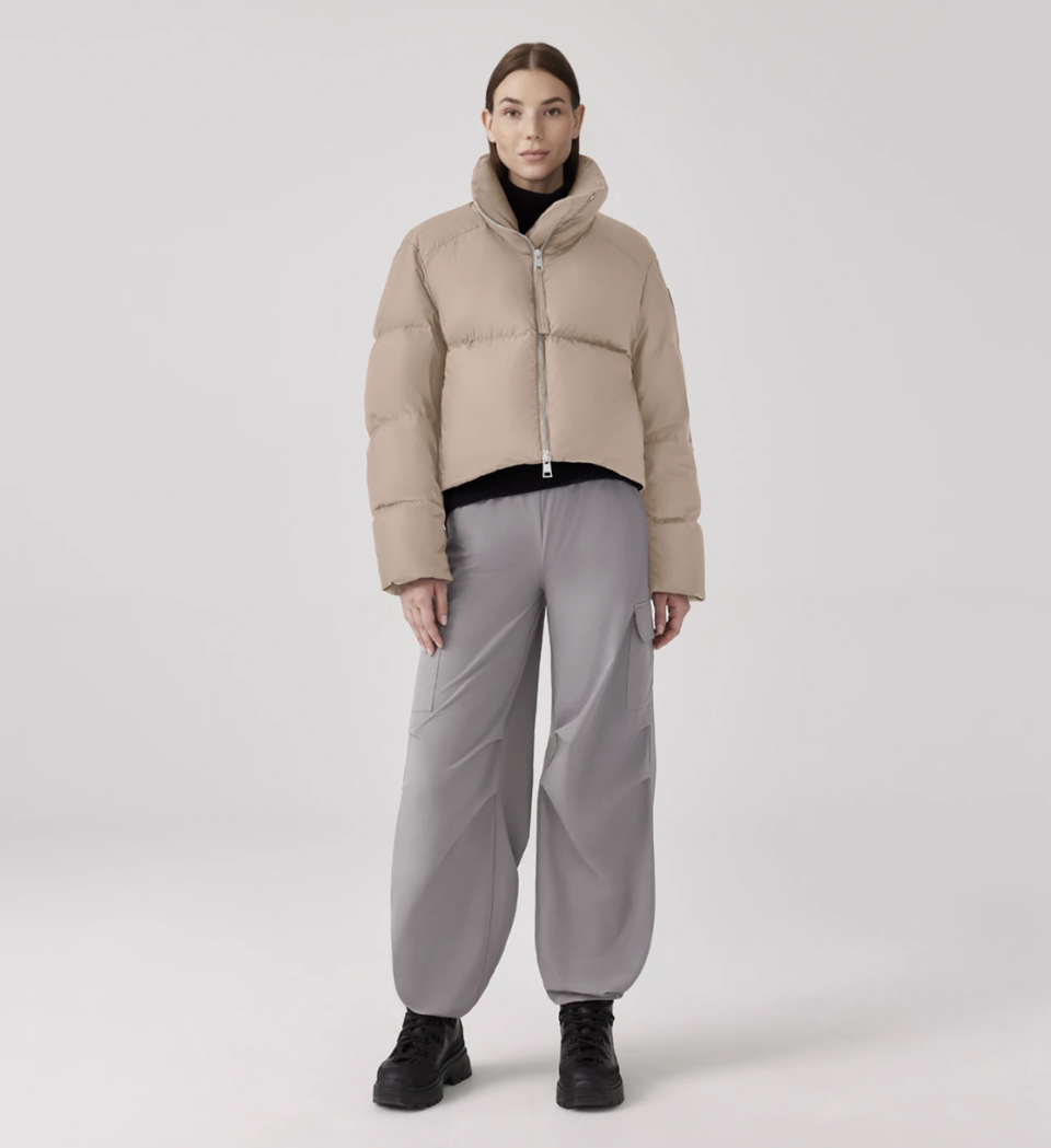 brunette model wearing grey pants and Garnet Cropped Puffer in Desert Sand (Photo via Canada Goose)