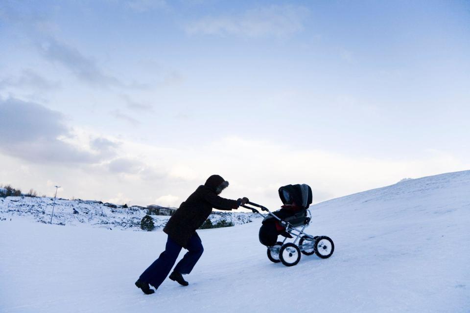 Una mujer empujando un carrito en la nieve.