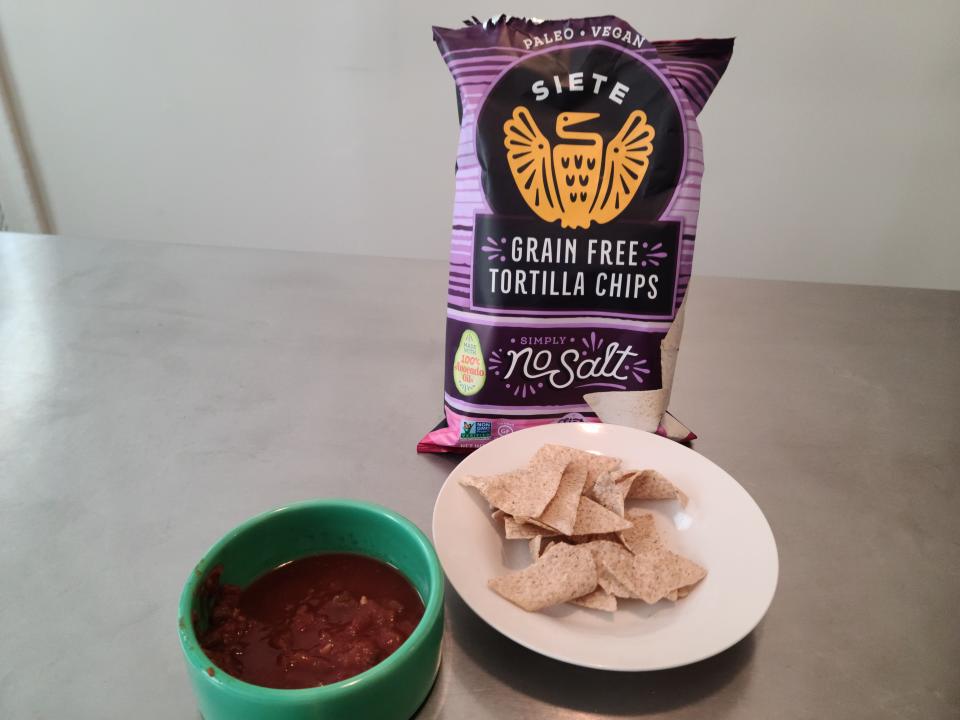 Bag of Siete no salt chips, chips on a plate next to a small bowl of red salsa.