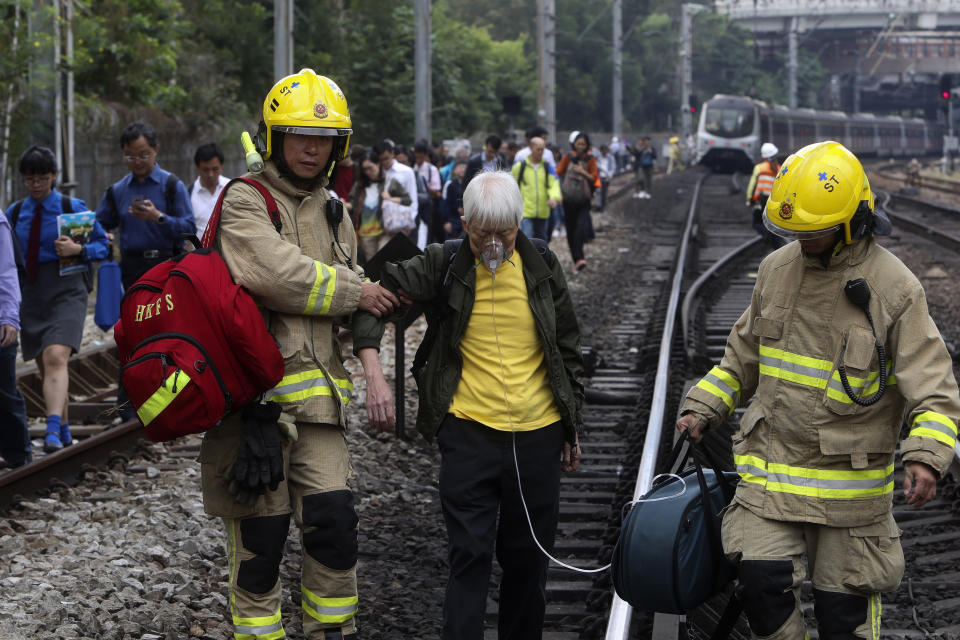 Firefighters help an elderly woman as commuters walk on the railway after their train service is disrupted by pro-democracy protesters in Hong Kong, Tuesday, Nov. 12, 2019. Protesters disrupted the morning commute in Hong Kong on Tuesday after an especially violent day in the Chinese city that has been wracked by anti-government protests for more than five months. (AP Photo)