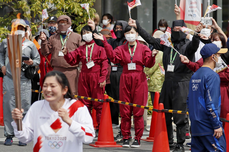 Spectators wearing face masks and ninja outfits, cheer a torchbearer carrying the Olympic torch in Iga, Mie prefecture, central Japan, Thursday, April 8, 2021. Tokyo, the capital of Japan, has asked the central government for permission to implement emergency measures to curb a surge in a rapidly spreading and more contagious coronavirus variant, just over three months before the start of the Olympics. (Kyodo News via AP)