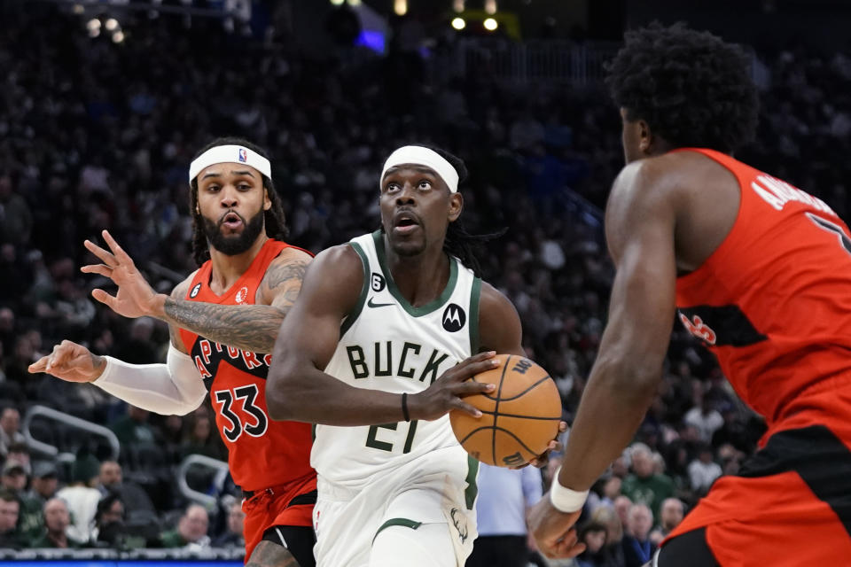 Milwaukee Bucks' Jrue Holiday, middle, drives to the basket between Toronto Raptors' Gary Trent Jr., left, and O.G. Anunoby during the second half of an NBA basketball game Sunday, March 19, 2023, in Milwaukee. (AP Photo/Aaron Gash)