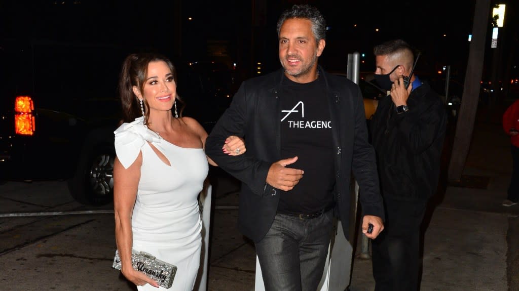 Kyle Richards in a white dress walking arm in arm with Mauricio Umansky who is wearing jeans and a black t-shirt