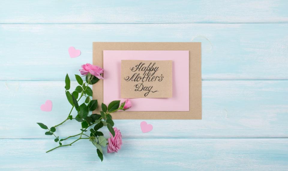 handmade card with the message mothers day on a painted pale blue table with pink roses