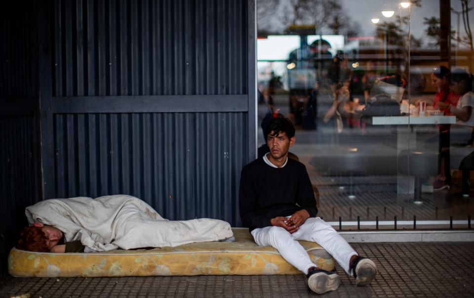 Homeless people rest on a mattress as customers eat inside a fast food restaurant at Retiro Rail Station on December 05, 2023 in Buenos Aires, Argentina