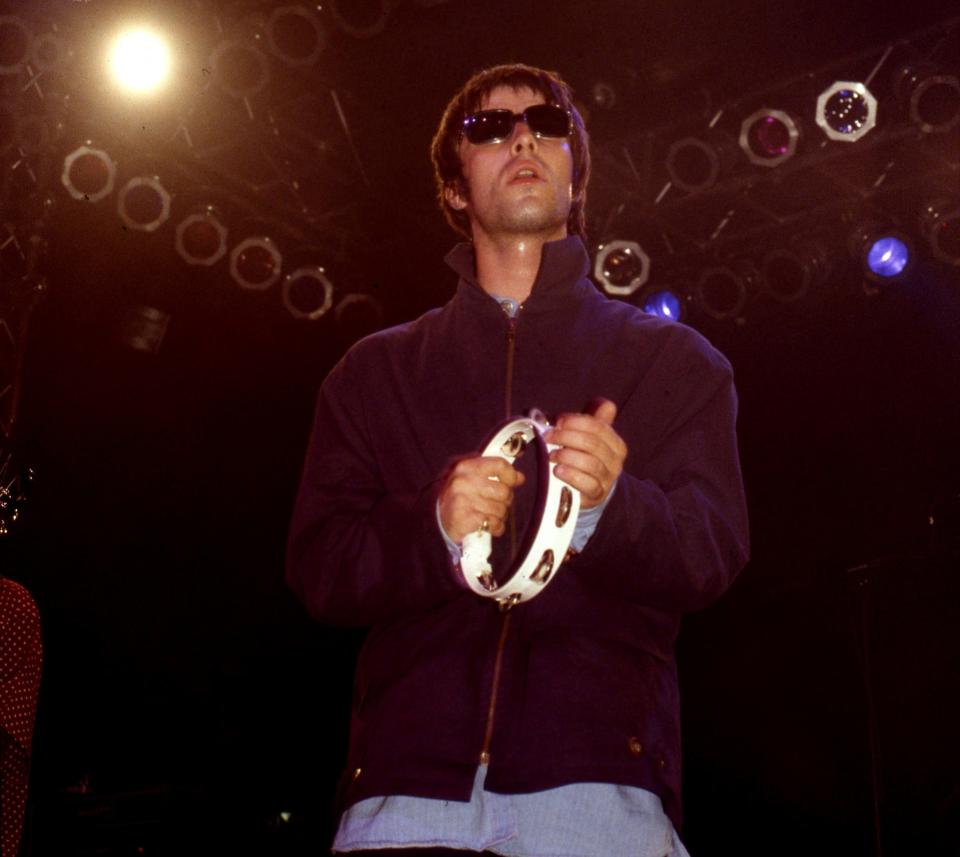 Liam Gallagher playing the tambourine on stage