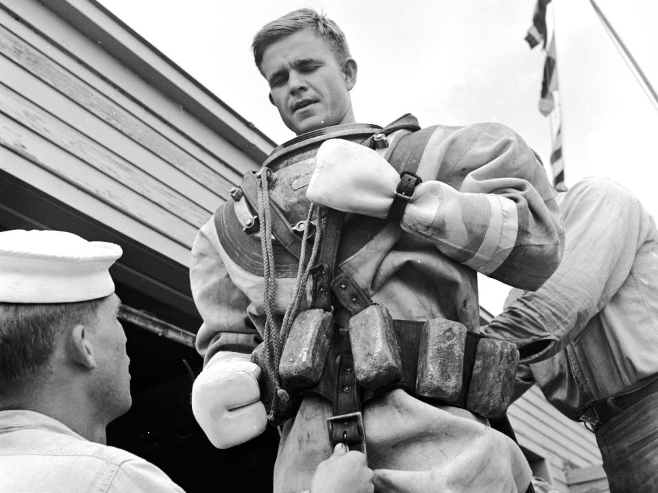 A US navy diver being fitted with a weight belt of about 100 pounds before a dive in 1955.