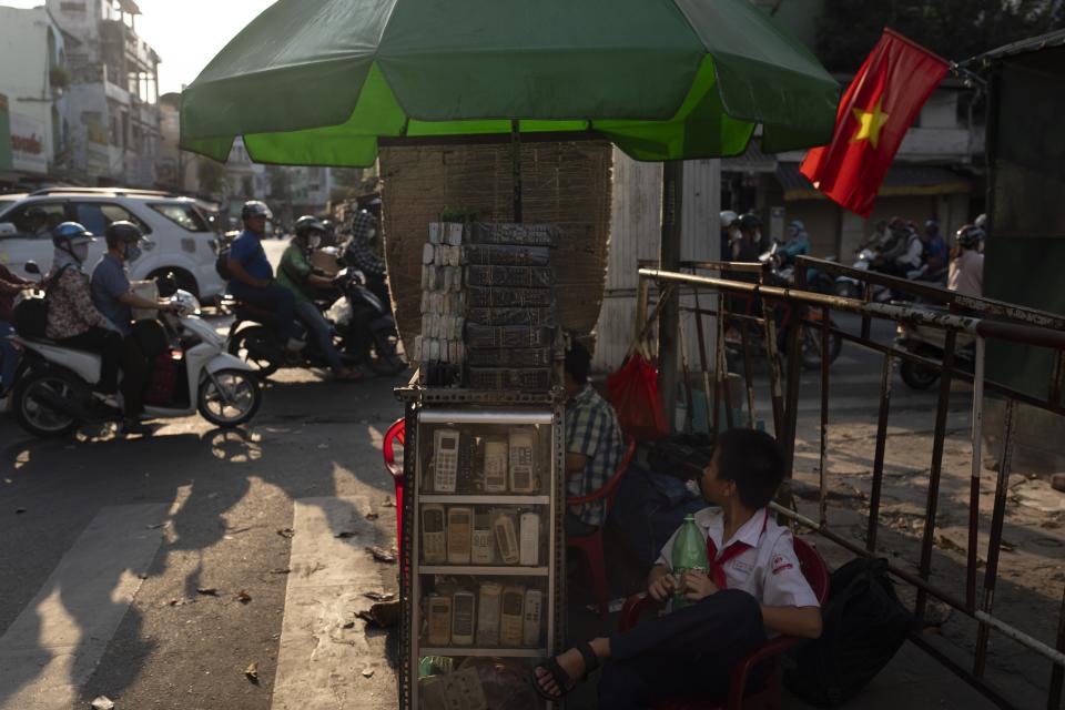 A boy in a school uniform sits next to a vendor selling used remote controls for various home appliances in Nhat Tao market, the largest informal recycling market in Ho Chi Minh City, Vietnam, Wednesday, Jan. 31, 2024. (AP Photo/Jae C. Hong)