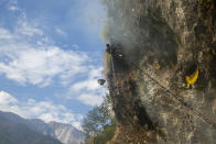 Devi Bahadur Nepali, an experienced honey hunter climbs on a bamboo rope to harvest cliff honey in Dolakha, 115 miles east of Kathmandu, Nepal, Nov. 19, 2021. High up in Nepal's mountains, groups of men risk their lives to harvest much-sought-after wild honey from hives on cliffs. (AP Photo/Niranjan Shrestha)