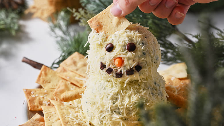 hand eating snowman cheese ball on plate with crackers