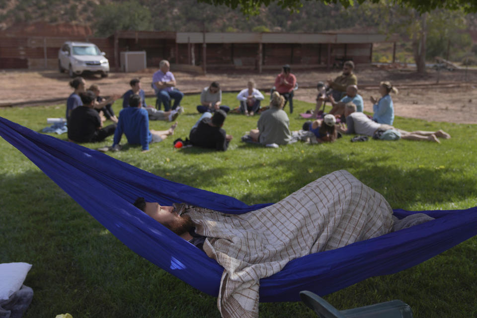 A Hummingbird Church retreat participant lays in a hammock while an integration circle takes place on the grass behind him, discussing the previous night's ayahuasca ceremony, in Hildale, Utah, on Sunday, Oct. 16, 2022. (AP Photo/Jessie Wardarski)