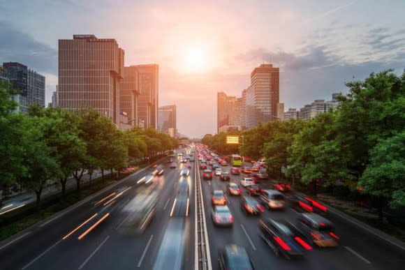 Picture of a setting sun behind a city skyline with a highway full of cars below.