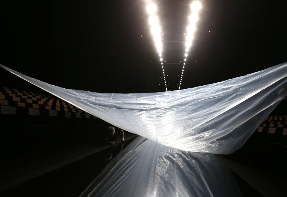 A protective plastic tarp is lifted into place as a worker prepares the runway before the Monique Lhuillier Fall 2013 collection is modeled during Fashion Week, Saturday, Feb. 9, 2013 in New York. (AP Photo/Jason DeCrow)