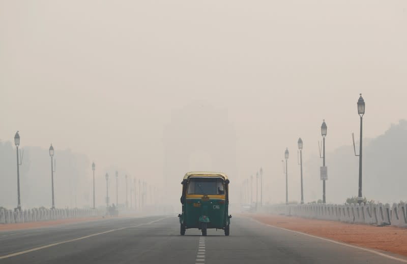 An auto-rickshaw moves past the India Gate on a smoggy morning in New Delhi