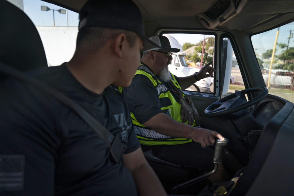 Student driver Luis Barrientos, foreground, listens to instructor Daniel Osborne while sitting in a practice truck at California Truck Driving Academy in Inglewood, Calif., Monday, Nov. 15, 2021. Amid a shortage of commercial truck drivers across the U.S., a Southern California truck driving school sees an unprecedented increase in enrollment numbers. The increase is big enough that the school is starting an evening class to meet the demand, according to Tina Singh, owner and academy director of California Truck Driving Academy. "I think that's only going to continue because there's a lot of job opportunities. We have over 100 active jobs on our job board right now," said Singh. The companies that normally would not hire drivers straight out of school are "100 percent" willing to hire them due to shortage issues, the director added. (AP Photo/Jae C. Hong)