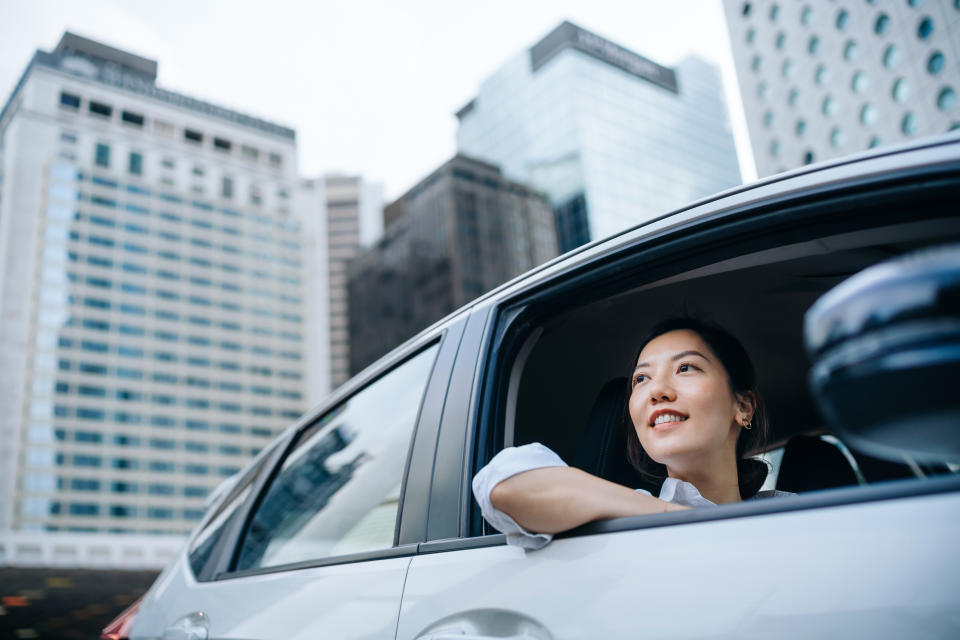 Woman leans out of a car window, smiling while looking at tall city buildings in the background