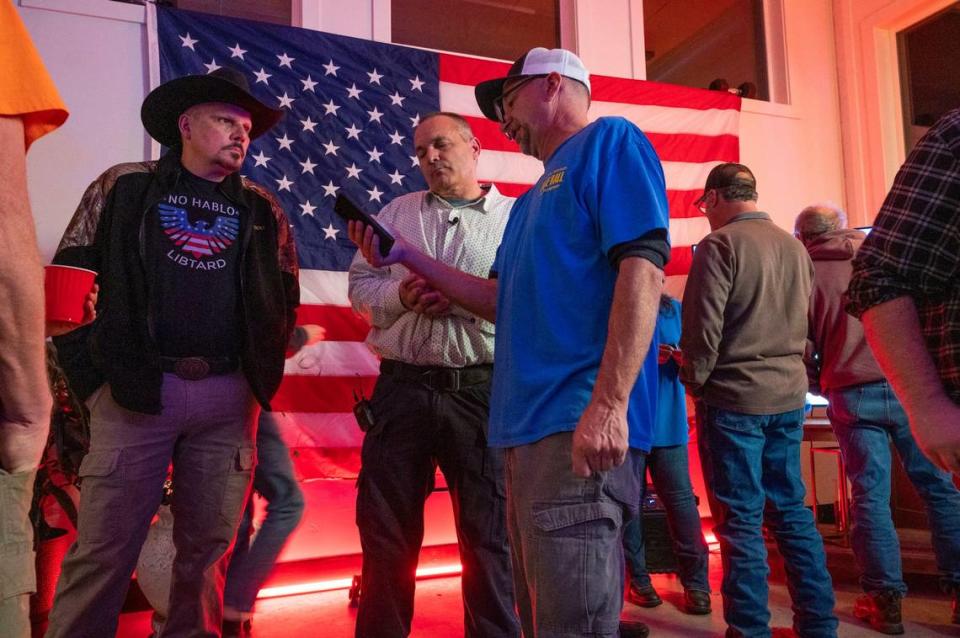 Shasta County Board of Supervisors candidate Dale Ball, center, shows his phone to District 4 Supervisor Patrick Jones as they await election results in 2022. At left, a man in a cowboy hat wears a shirt that reads “No Hablo Libtard.”