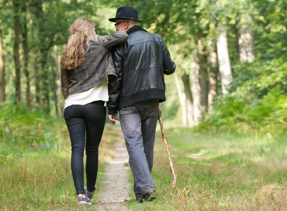 A couple walks arm-in-arm down a forest path