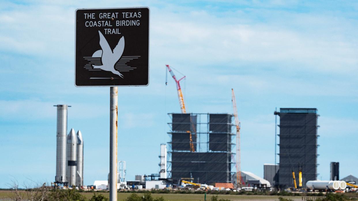  a sign that says 'the great texas coastal birding trail' stands in front of spacex hardware and pieces of spacex starship, all far in the background 