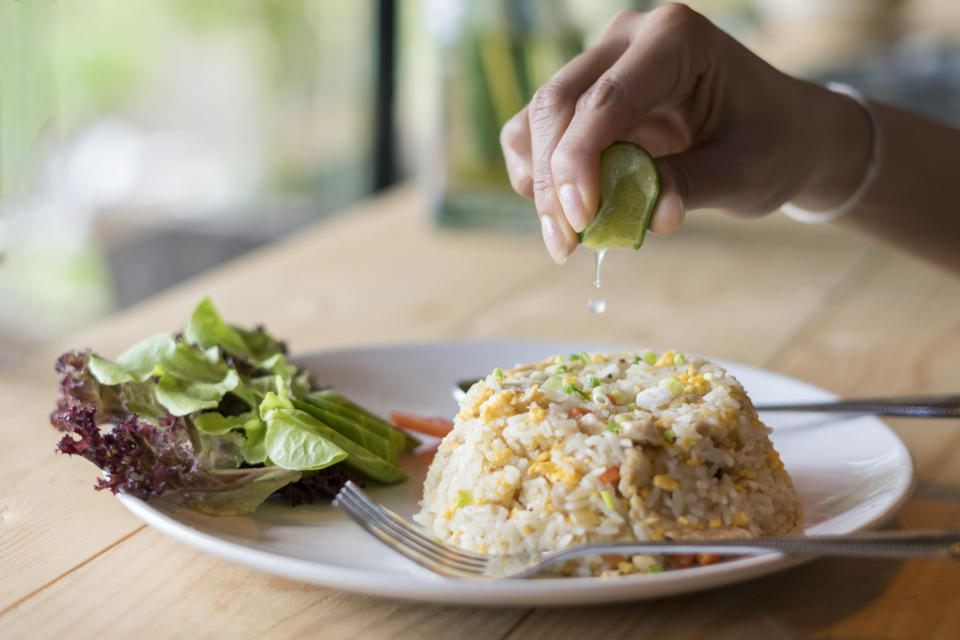 Person squeezing lime on fried rice with vegetables next to a salad