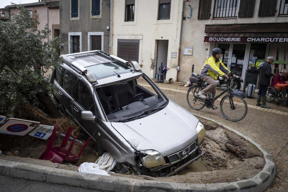 Un hombre conduce una bicicleta frente a un auto dañado en el pueblo de Villegailhenc, suroeste de Francia, el lunes 15 de octubre de 2018. (AP Foto/Fred Lancelot)