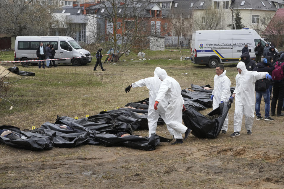 FILE - Men wearing protective gear carry a dead body during the exhumation of killed civilians in Bucha, outskirts of Kyiv, Ukraine, Friday, April 8, 2022. Police are investigating the killings of more than 12,000 Ukrainians nationwide in the war Russia is waging, the national police chief said Monday. In the Kyiv region near Bucha, authorities showed several victims whose hands were tied behind their backs. (AP Photo/Efrem Lukatsky, FILE)