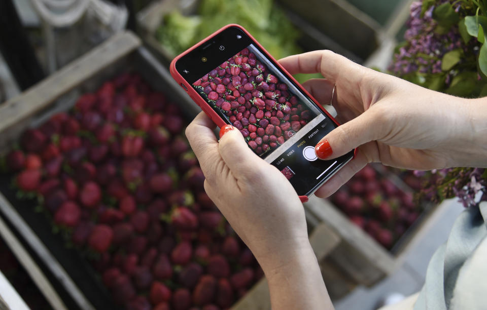 This April 10, 2019 photo shows Gaby Dalkin taking a photo of strawberries at Santa Monica Downtown Farmers Market in Santa Monica, Calif. Dalkin, the chef behind the popular Website and social media accounts, What’s Gaby Cooking, is forging her own path. Every Monday she posts a live demo to Instagram as she cooks dinner which has become appointment viewing for some fans. Her husband films it and reads questions from viewers as she’s cooking. (AP Photo/Chris Pizzello)