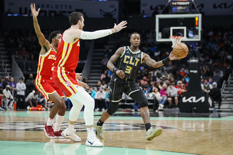 Charlotte Hornets guard Terry Rozier, right, passes the ball around the defense of Atlanta Hawks guard Trent Forrest, left, and forward Frank Kaminsky, center, during the first half of an NBA basketball game Friday, Dec. 16, 2022, in Charlotte, N.C. (AP Photo/Rusty Jones)
